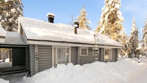 Uma cabana de tronco com telhado coberto de neve, rodeada por árvores carregadas de neve.