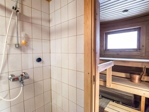 Shower area features a handheld showerhead and handheld shower attachment, set against a backdrop of light-colored tiles.