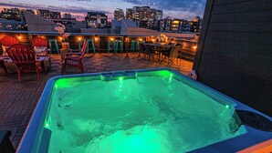 Una vasca idromassaggio sul tetto con illuminazione verde, circondata da posti a sedere all'aperto e vista sulla città.
