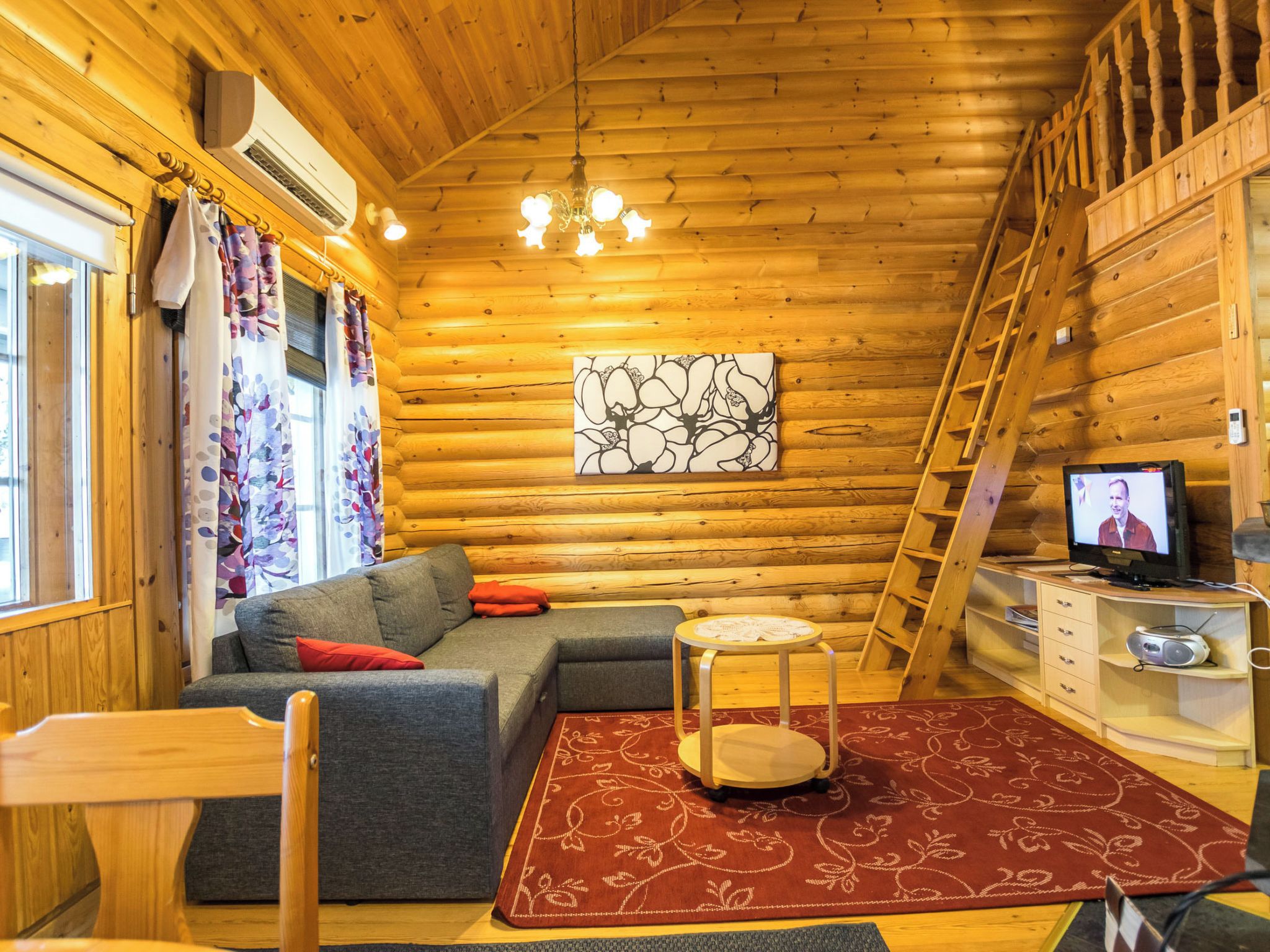 A cozy log cabin interior with a sofa, a small round table, a television, and a ladder.