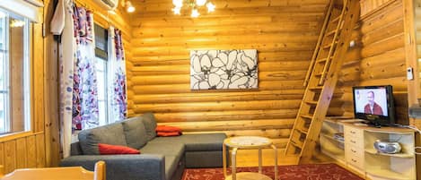 A cozy log cabin interior with a sofa, a small round table, a television, and a ladder.