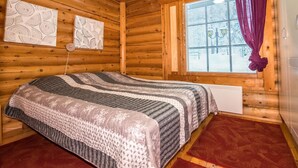 Camera da letto in una baita di legno con un letto, una finestra con persiane e una tenda rossa.