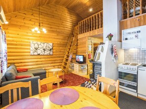 Acogedor interior de cabaña de troncos con sala de estar, cocina y habitación doble en un altillo.