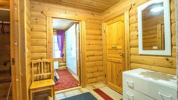 Interior de uma cabana de madeira com uma cadeira de madeira, um penteado branco e um espelho na parede.