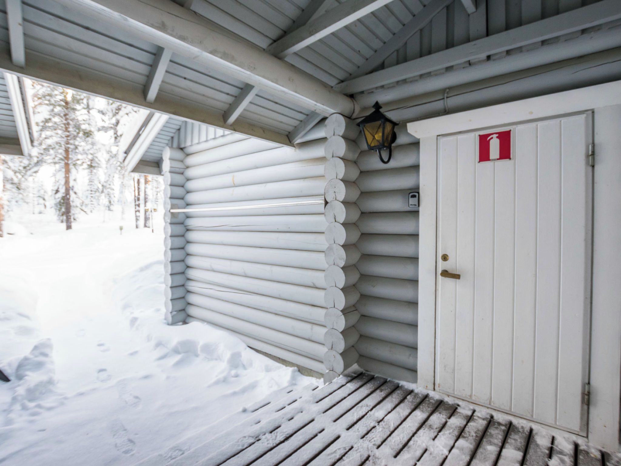 Et sneklædt træhus med en hvid dør og et rødt nødudgangsskilt.