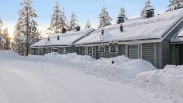 Fileira de cabanas de toras com telhados cobertos de neve, céu claro e estrada coberta de neve.