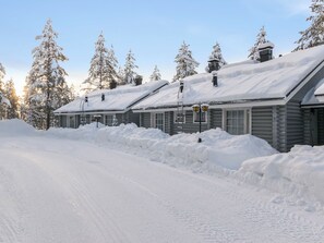 Una hilera de cabañas de madera con techos nevados, cielo despejado y un camino cubierto de nieve.