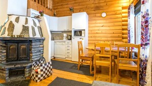 L'interno accogliente di un rifugio con camino in pietra, tavolo da pranzo in legno e angolo cottura.