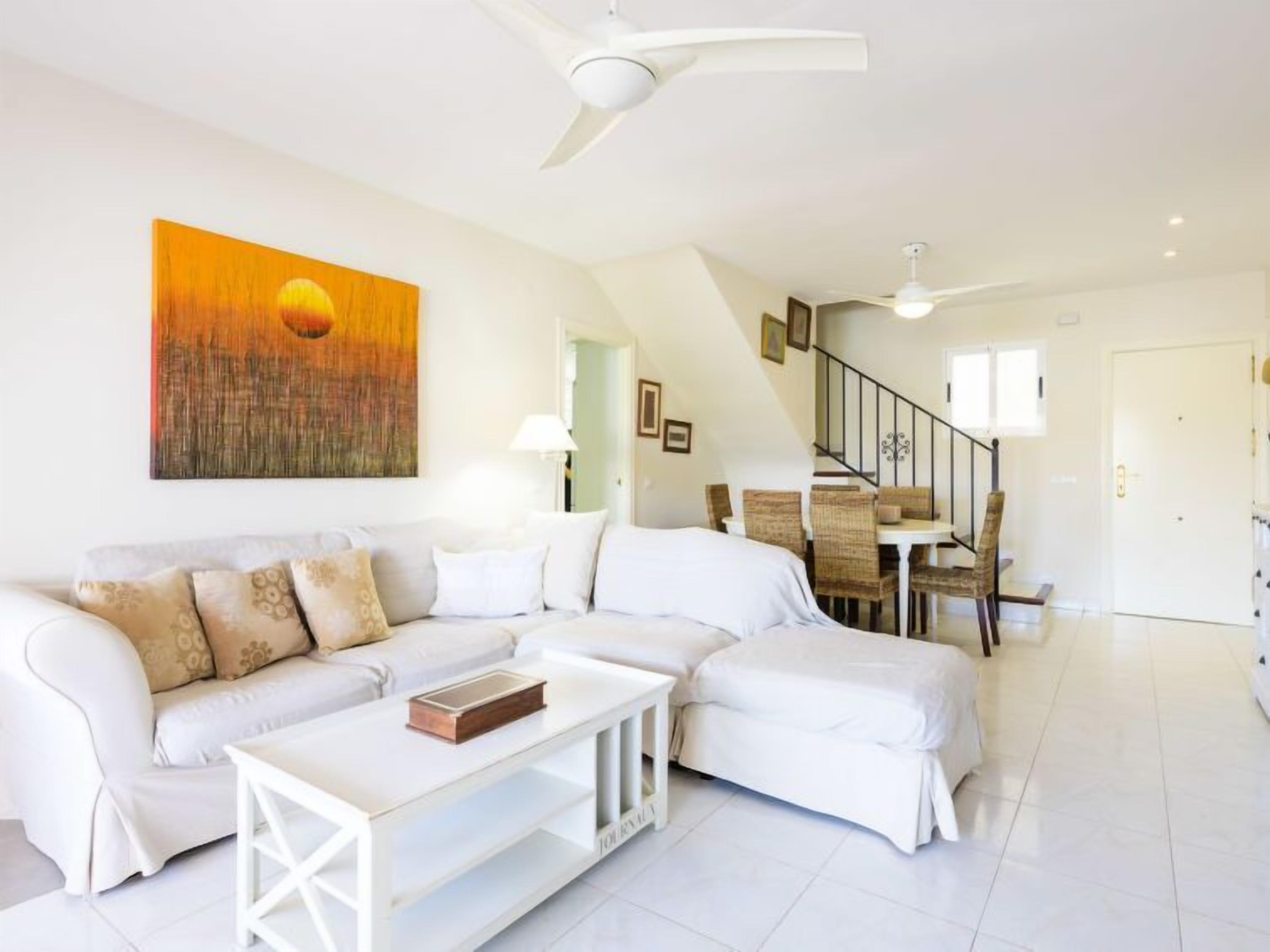 A modern living room with a white sectional sofa, a coffee table, and a dining area with wicker chairs and a table.