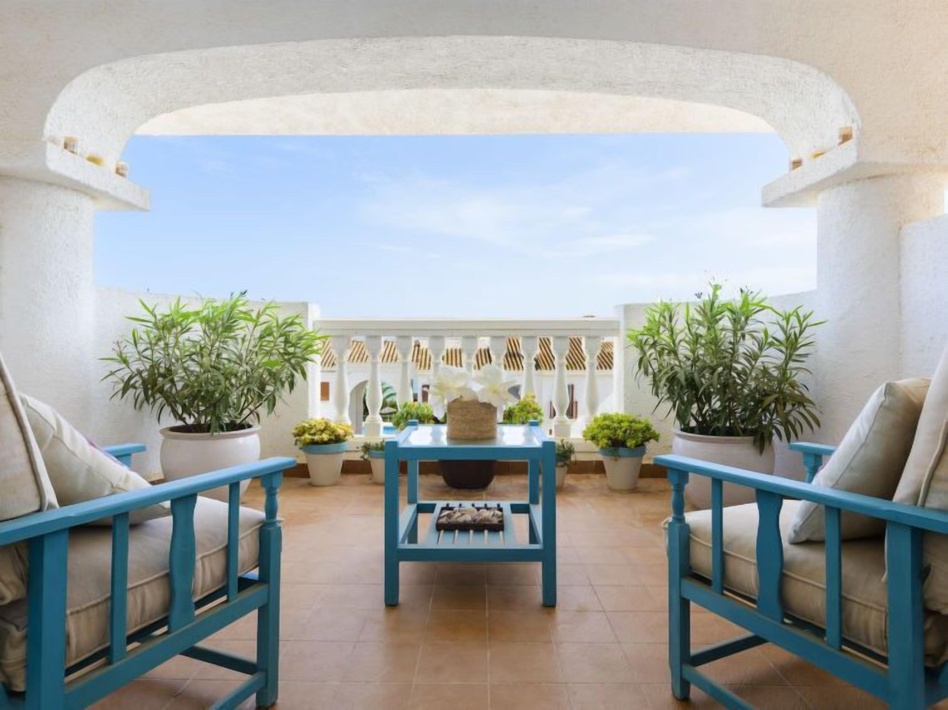 A terrace with a white archway, blue furniture, and potted plants.