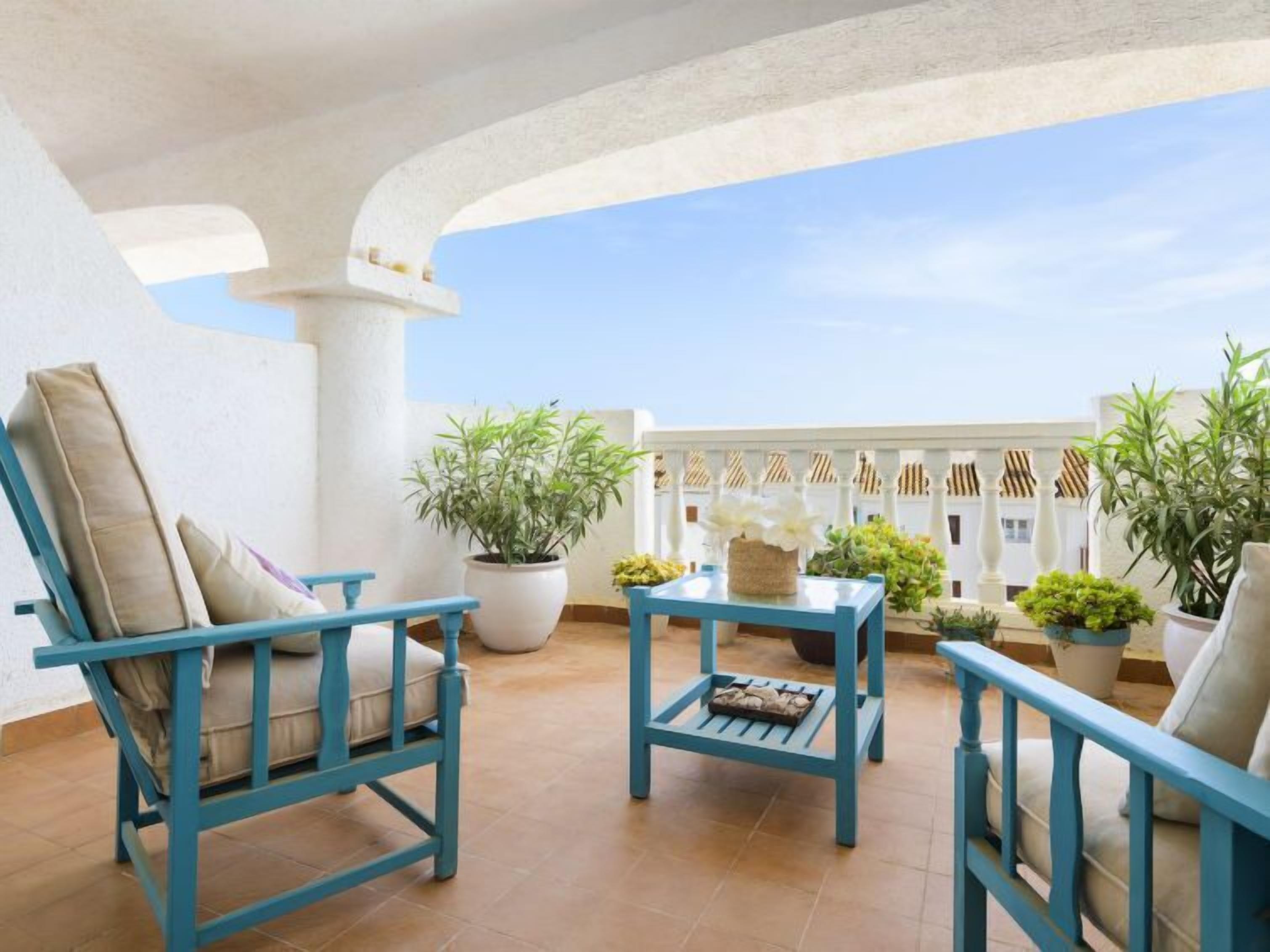 A terrace with blue furniture, potted plants, and a white balustrade.