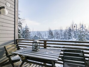 A wooden bench and table on a porch with a view of snow-covered trees.