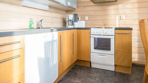 A modern kitchen with wooden cabinets, a built-in microwave, a coffee maker, and a stove. - Rinteenkotka mökki by Interhome (Hyrynsalmi)