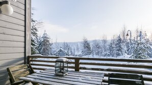 A wooden deck with a bench and a table, overlooking a snowy landscape with trees and a cabin. - Rinteenkotka mökki by Interhome (Hyrynsalmi)