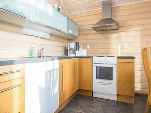 A modern kitchen with wooden cabinets, a built-in oven, a coffee maker, and a stainless steel range hood. - Rinteenkotka mökki by Interhome (Hyrynsalmi)