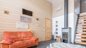 A cozy room with a wooden wall, a sofa, a rug, a fireplace, and a wooden ladder. - Rinteenkotka mökki by Interhome (Hyrynsalmi)