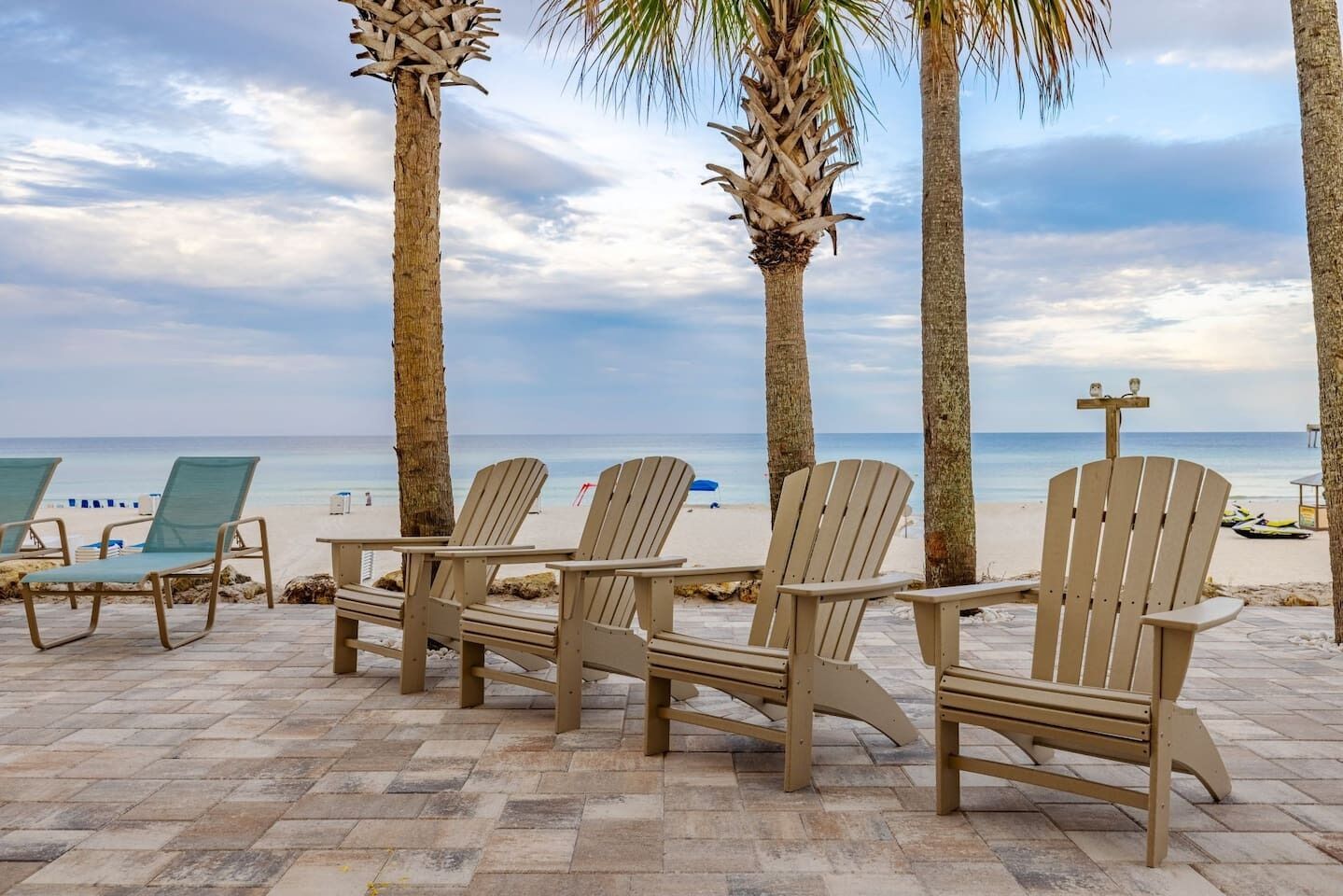 A beachside seating area with Adirondack chairs and palm trees.