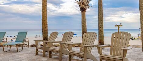 A beachside seating area with Adirondack chairs and palm trees.