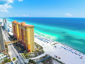 Ein Hochhaus-Hotel mit Blick auf den Strand, eine Straße mit Fahrzeugen und ein Sandstrand mit Sonnenschirmen.