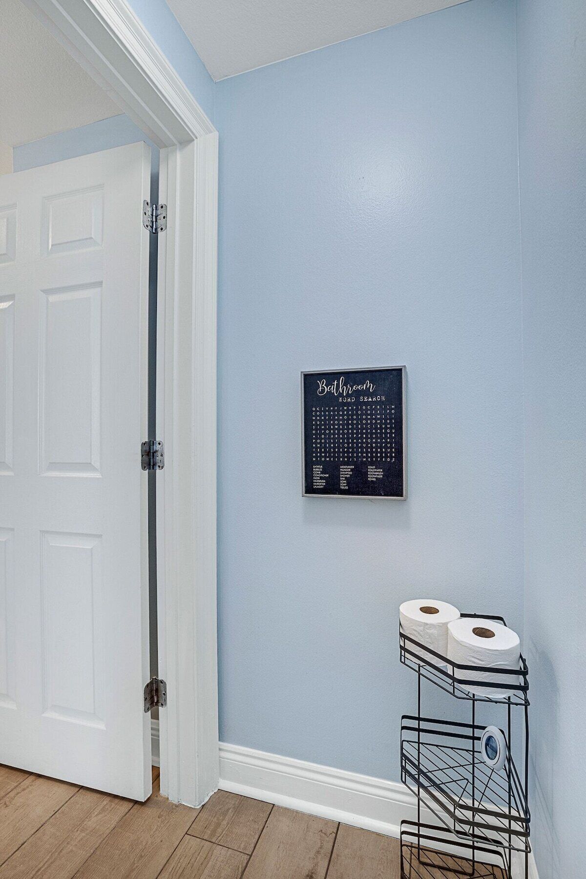 A bathroom with a toilet paper holder and a framed word search puzzle on the wall.