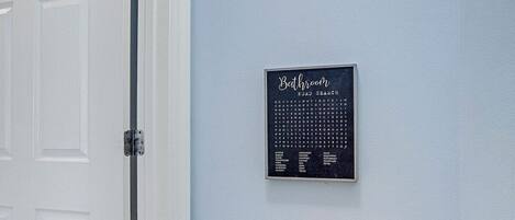 A bathroom with a toilet paper holder and a framed word search puzzle on the wall.
