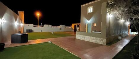 A well-lit outdoor area with a lawn, a paved walkway, and a building with a light fixture.