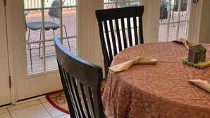 Una stanza con un tavolo rotondo e due sedie, vista su un terrazzo con mobili da esterno e un piccolo modellino di una casa sul tavolo.