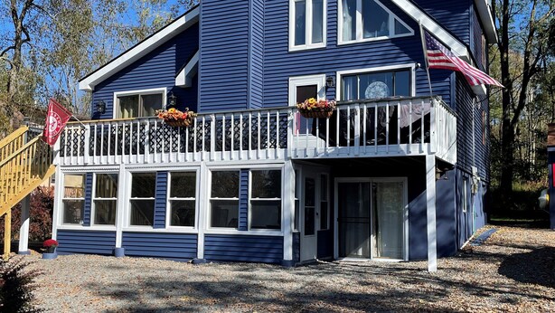 A two-story house with a white porch and a small deck, surrounded by trees and a gravel driveway. - Spacious and Tranquil Lazy Lake Lodge Escape (Lake Ariel)