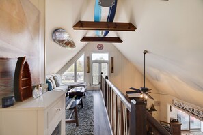 Relax in this charming attic space with a high ceiling, featuring a cozy seating area and a large window.