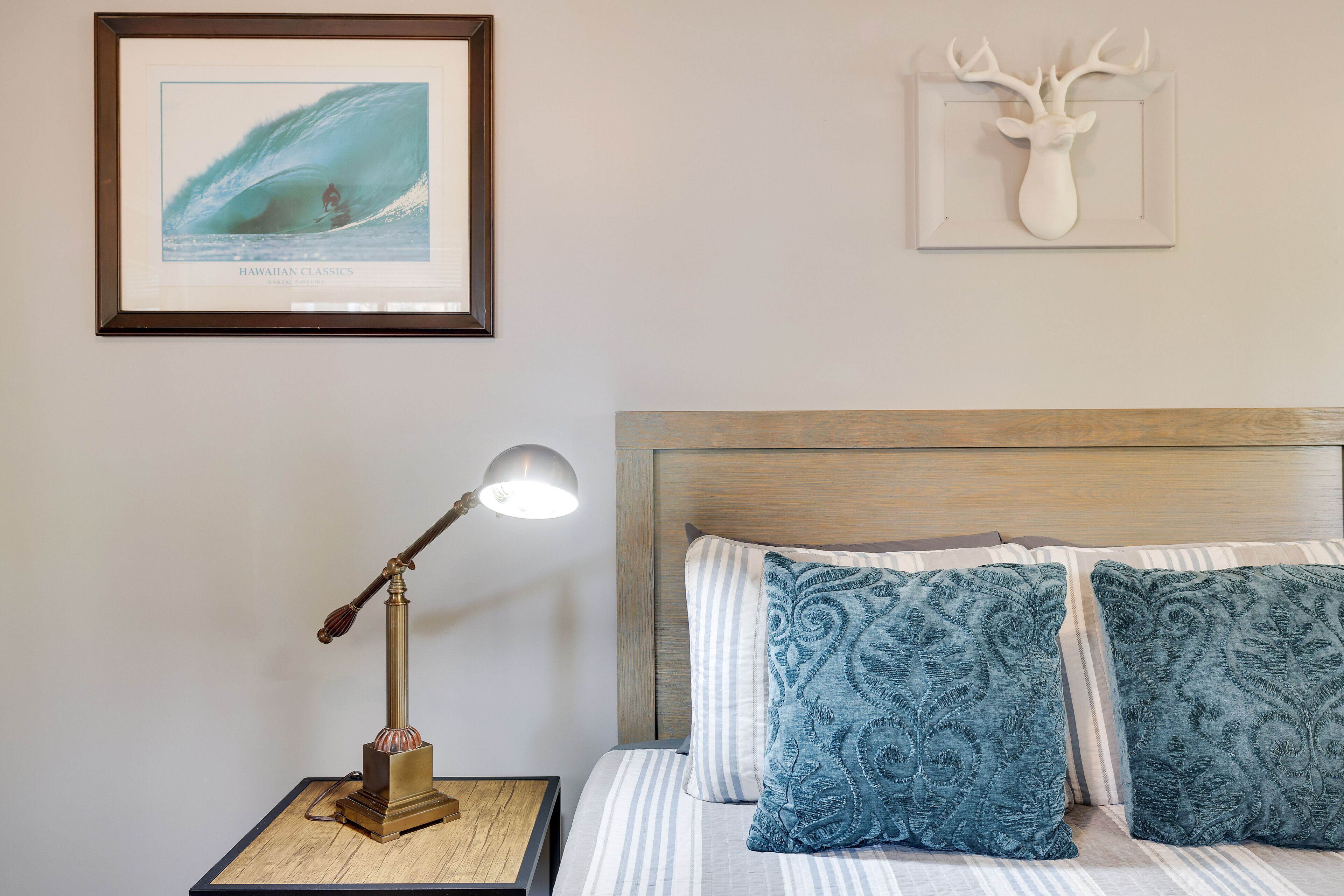 A neatly arranged bedroom with a bed, pillows, a framed picture, a lamp, and a wall-mounted deer head decoration.