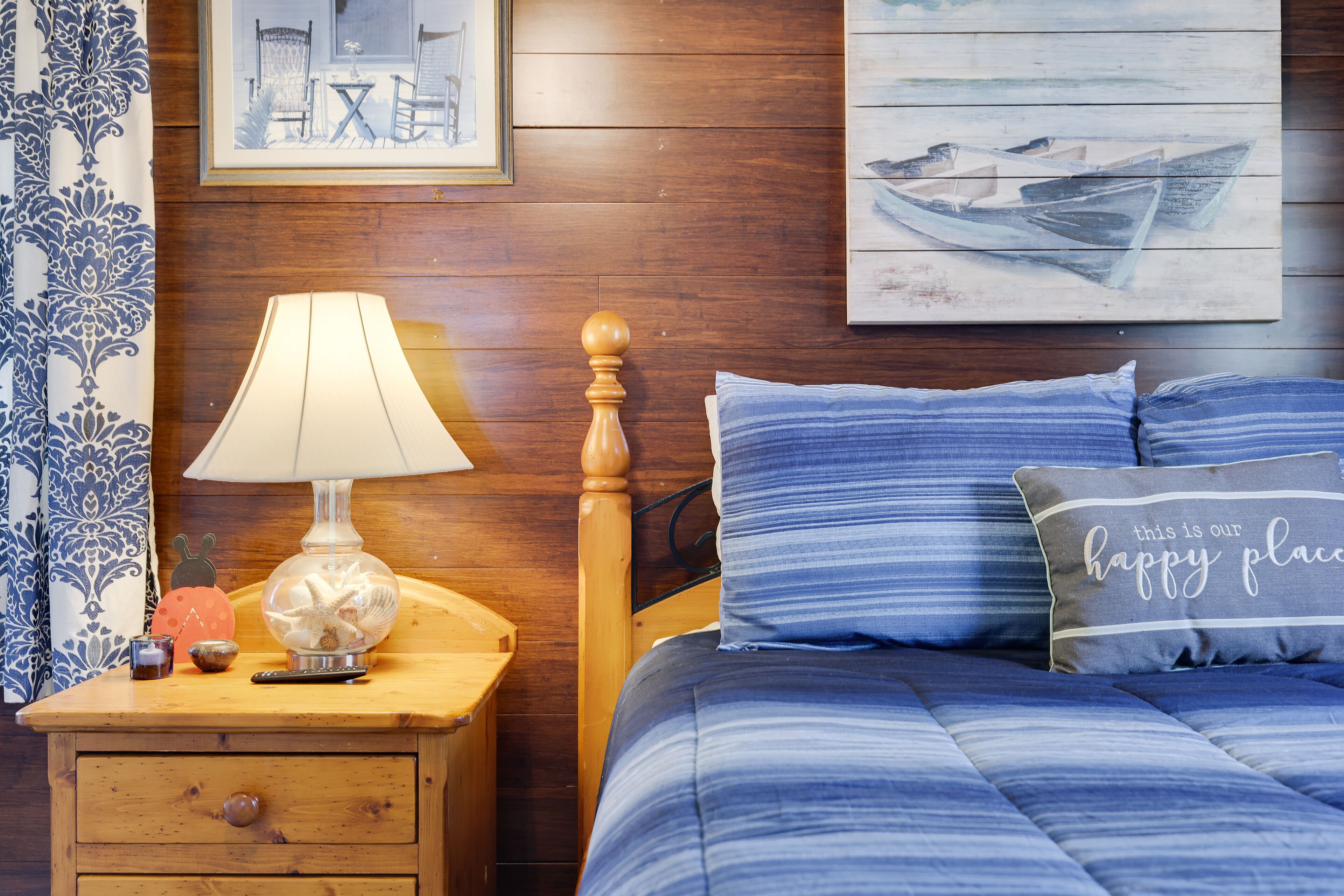 A bedroom with a wooden headboard, a blue-striped bedspread, a decorative lamp, and a nightstand with a drawer.