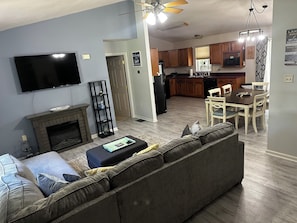 Una sala de estar con chimenea, televisor, sofá y comedor con mesa y sillas.