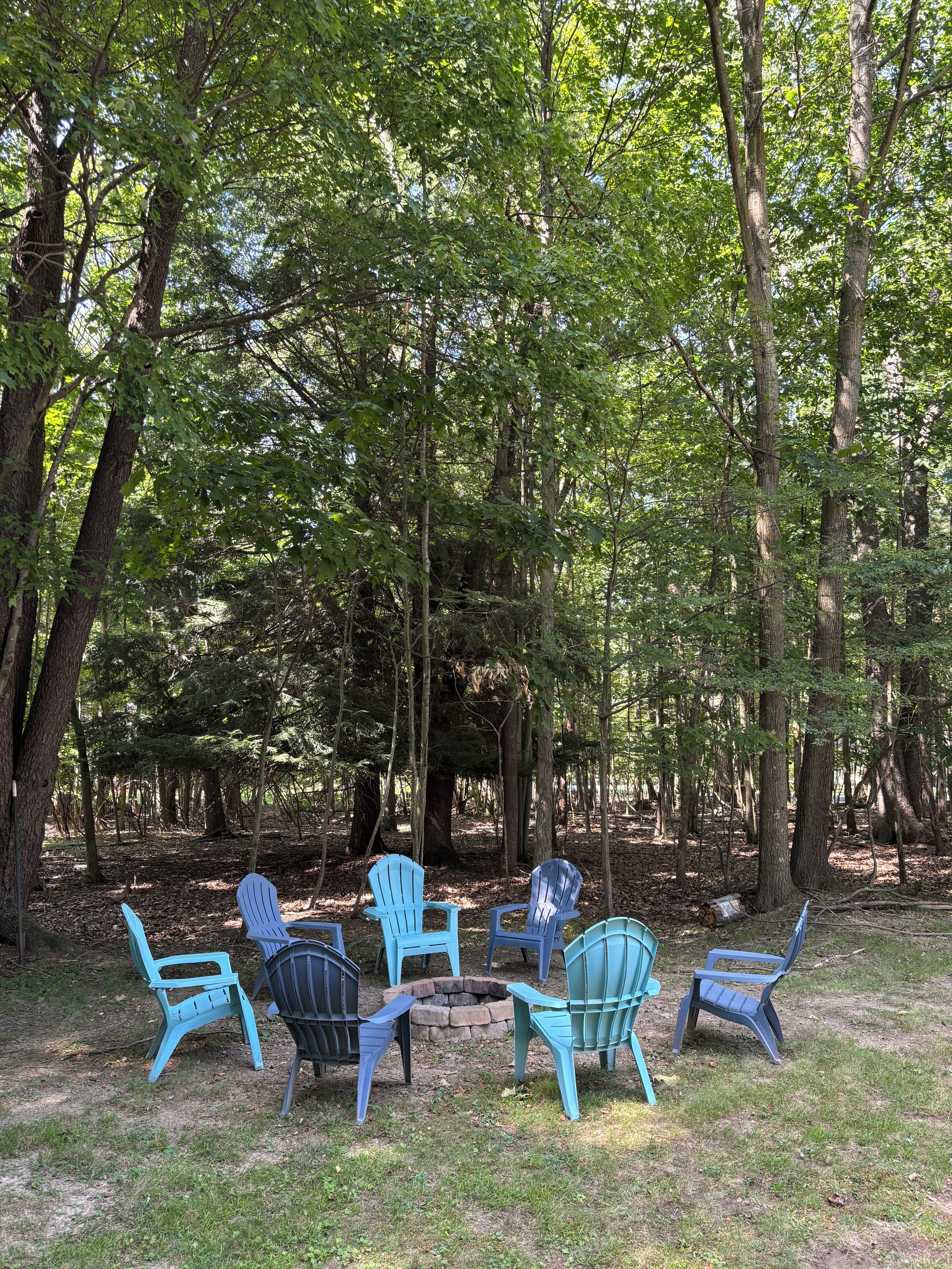 Un groupe de fauteuils Adirondack disposés en cercle sur une pelouse, entourée d’arbres.