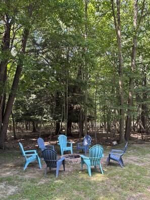 Un grupo de sillas Adirondack dispuestas en círculo sobre una zona cubierta de césped, rodeado de árboles.