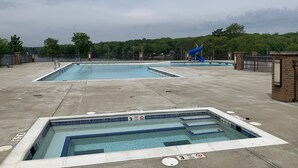 Zona de piscina con varias piscinas, un tobogán azul y un perímetro cercado.