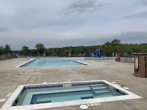 Zona de piscina con varias piscinas, un tobogán azul y un perímetro cercado.