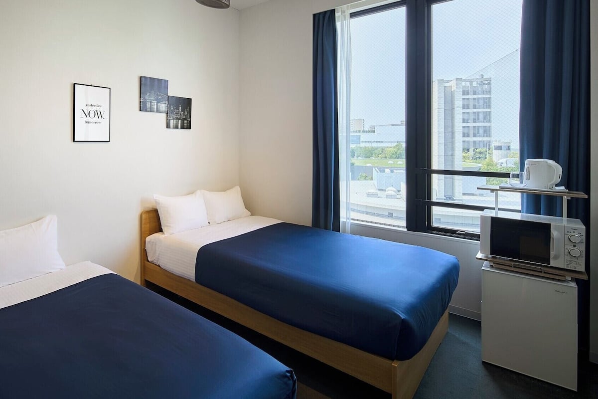 A hotel room with two beds, a microwave, and a window with a city view.