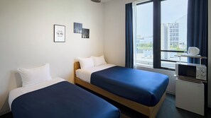 Une chambre d’hôtel avec deux lits, un four à micro-ondes et une fenêtre donnant sur la ville.