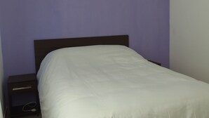 A bedroom with a bed, a nightstand, and a wall painted in a solid color.