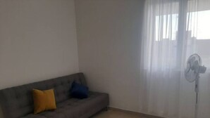 A living room with a grey sofa, a fan, and sheer curtains.