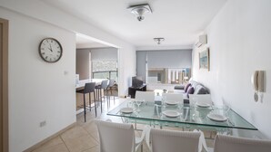 Un comedor moderno con una mesa de vidrio, sillas blancas y un reloj en la pared.