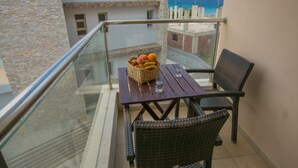 Un balcón con sillas de mimbre, una mesa de madera y una cesta de fruta.