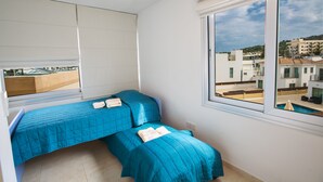 Un dormitorio con dos camas, un ventanal con vistas a edificios y un balcón.