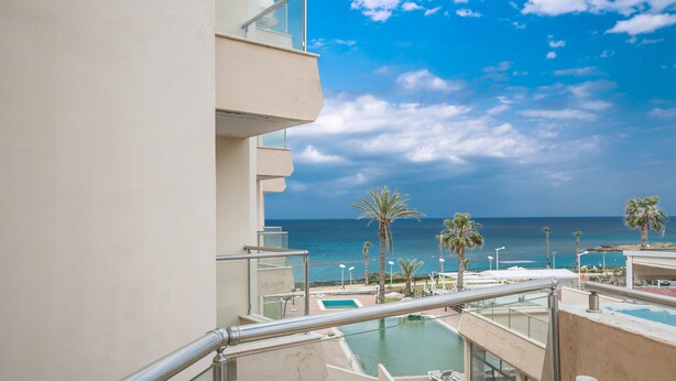 Un balcón con piscina, palmeras y vista al océano.