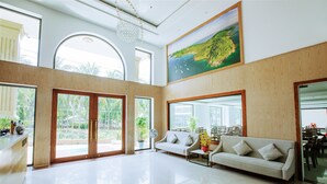 A spacious living room with a large sofa, a dining area with chairs, a large painting of a landscape, and a view of the outdoors through large windows. - Night Sea Hotel (Phu Quoc)
