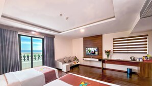 A hotel room with two beds, a sofa, a TV, a desk, and a balcony with a view. - Night Sea Hotel (Phu Quoc)