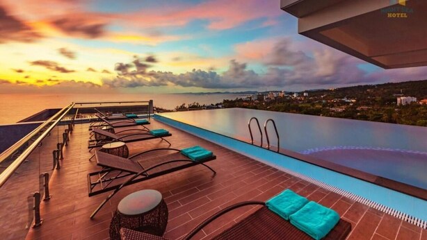 A rooftop infinity pool with lounge chairs and a view of the sea at sunset. - Night Sea Hotel (Phu Quoc)