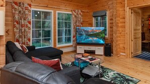 L’intérieur d’un chalet en bois, avec un canapé, un téléviseur et une petite table sur laquelle sont posés divers objets.