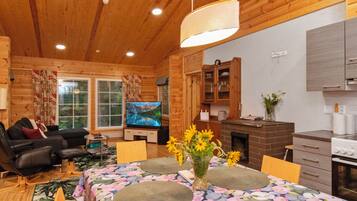 A cozy cabin interior with a dining area, a living room with a sofa and a TV, wooden walls, and a fireplace.
