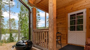 Une cabane en bois avec une véranda, un barbecue et une porte donnant sur l’intérieur.